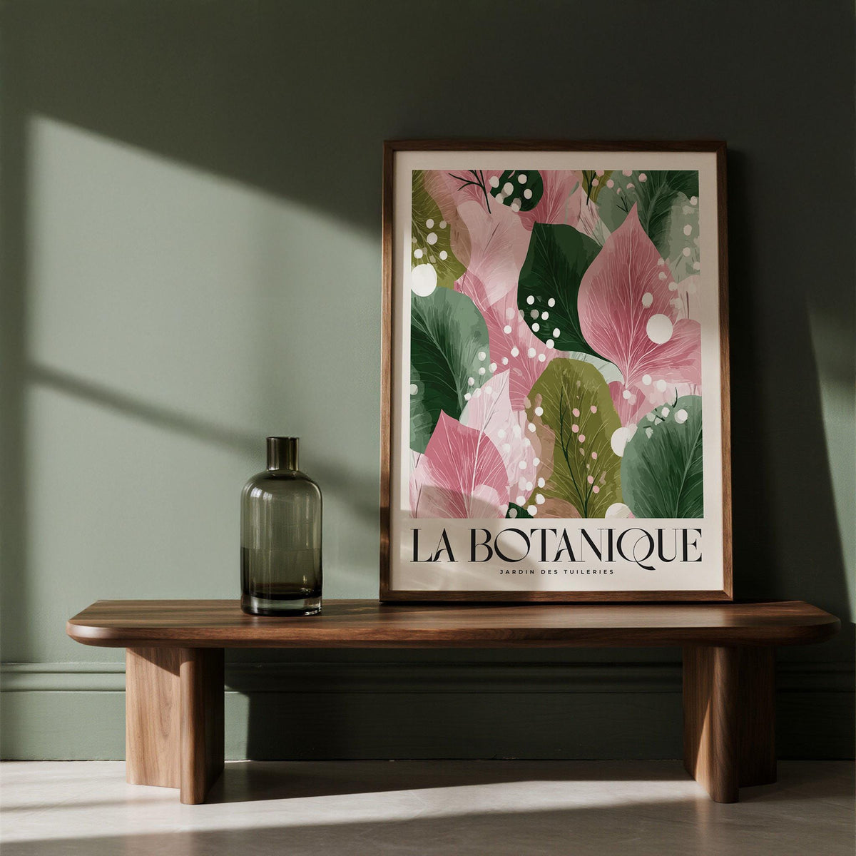 Framed floral abstract print with pink and green leaves leaning on a wooden bench with a glass vase