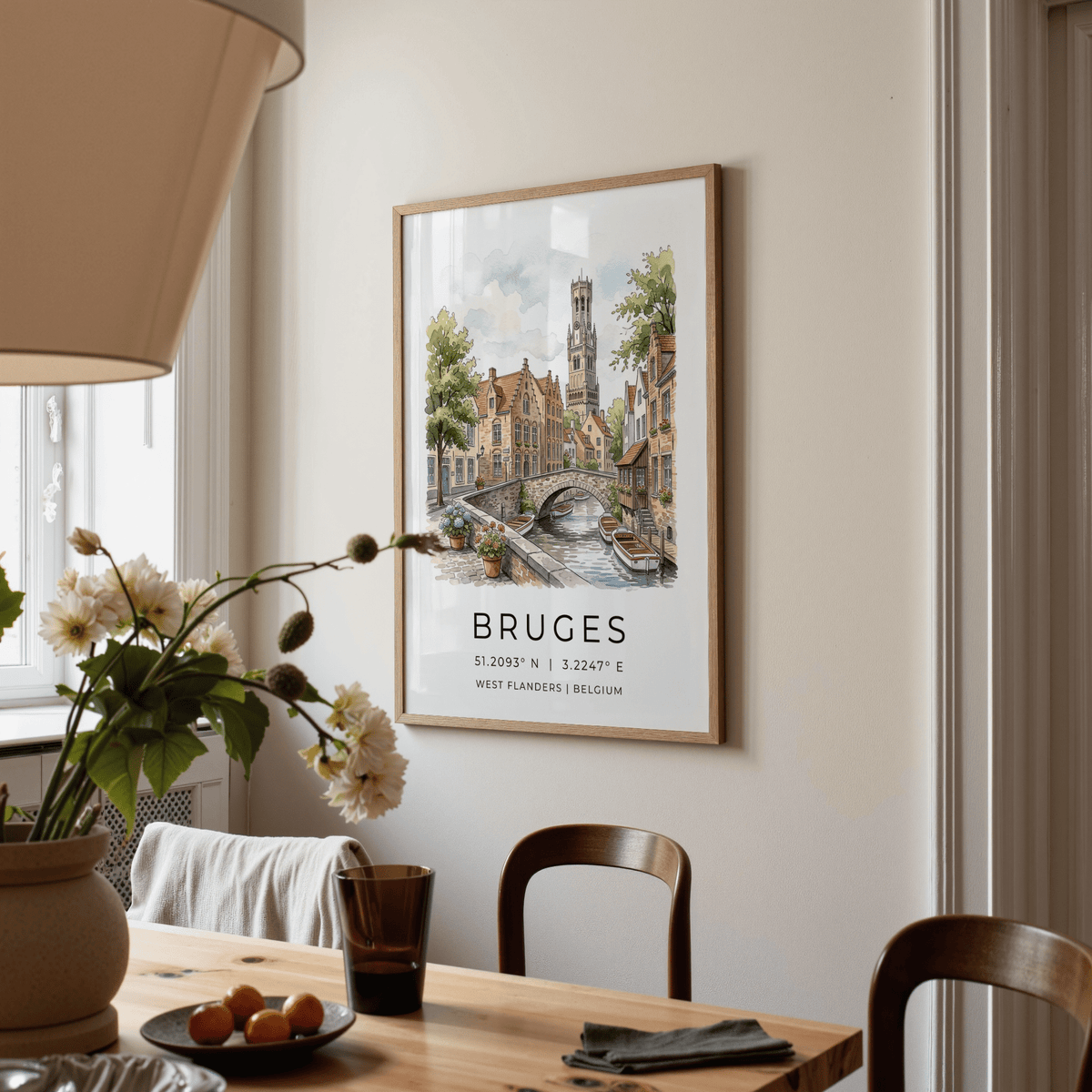 Bruges Canal Art Print hanging on cream wall above wooden dining table with chairs and vase of flowers