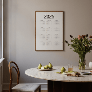 Minimalist wall calendar with black and beige text above a dining table with green apples and a vase of flowers