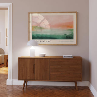 Framed pastel colored wall art above a mid-century wooden sideboard with a lamp and bowl