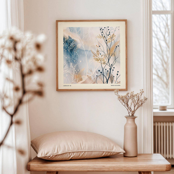 Neutral Prints abstract botanical artwork with blue and beige tones hanging above a wooden bench with cushion and vase
