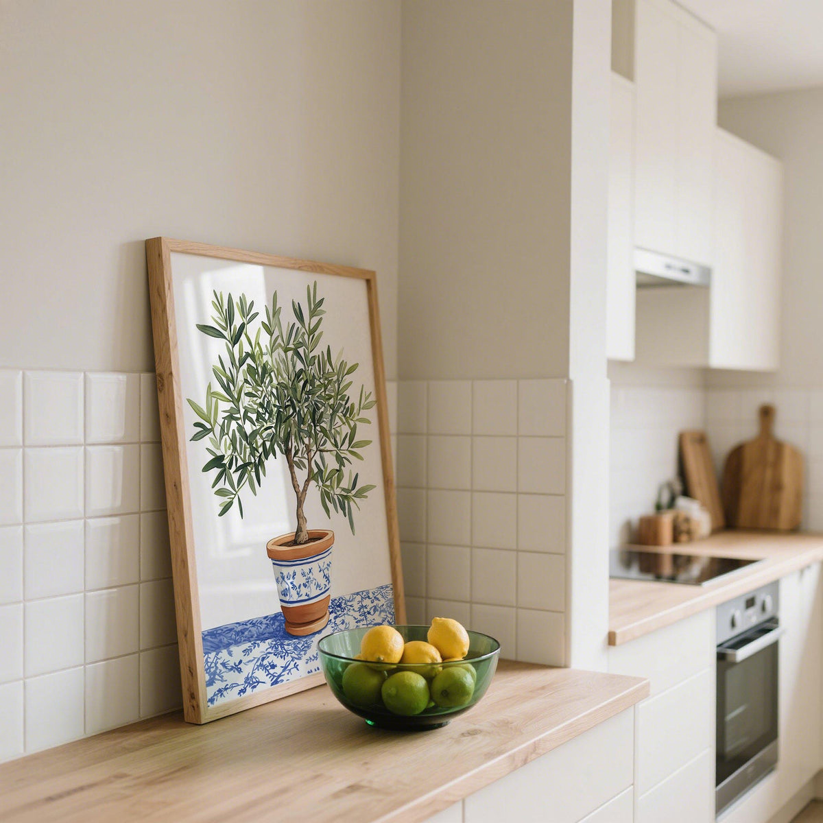 Print leaning on a kitchen counter of an olive tree in a terracotta pot with blue pattern next to a bowl of lemons and limes