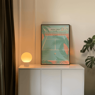 Framed Miami Beach Tennis Print leaning on white cabinet with a glowing round lamp