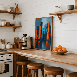 Print leaning on a wooden kitchen countertop featuring an abstract city skyline in blue and orange hues with a bowl of oranges nearby