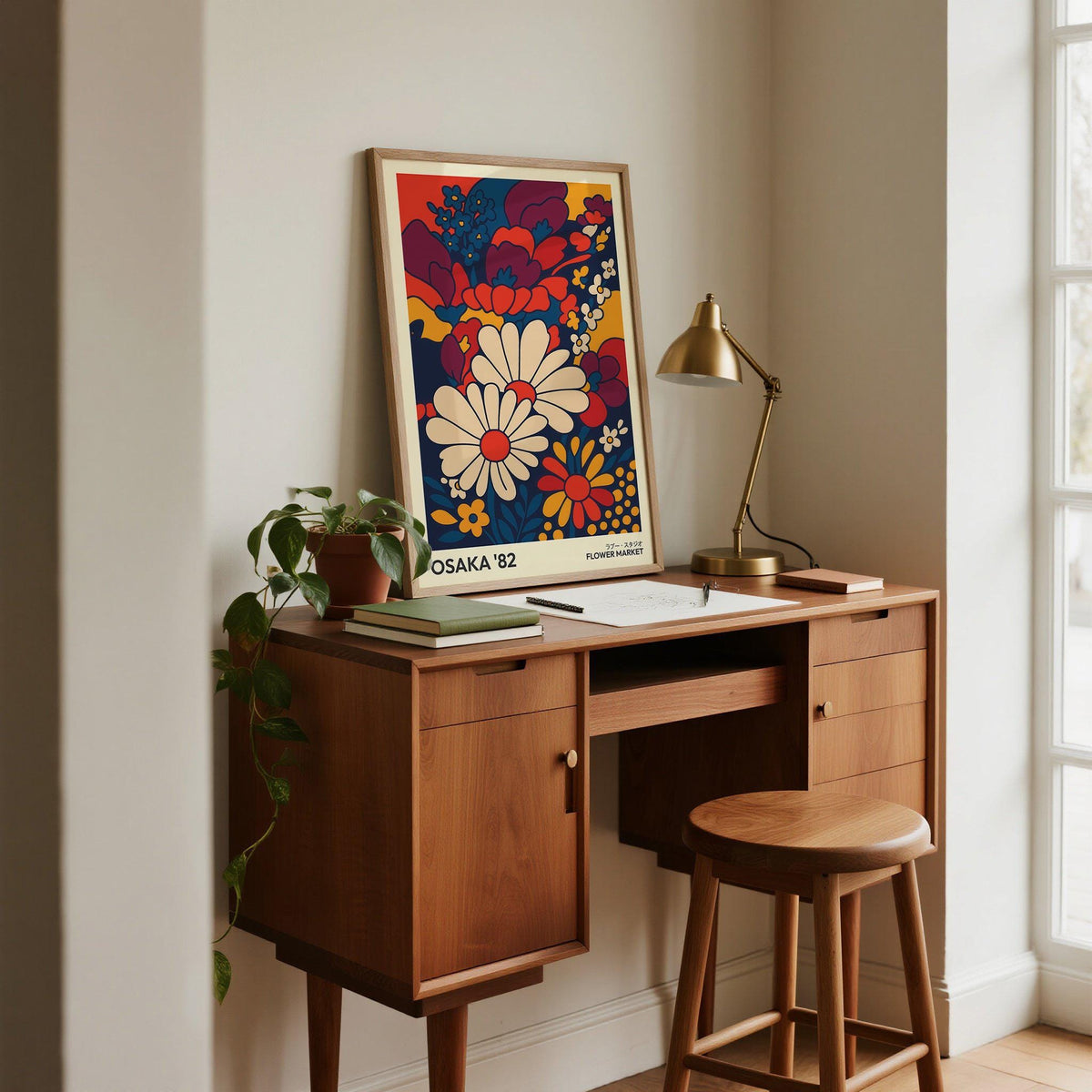 Print leaning on a wooden desk of daisies in retro mid-century style with navy and red hues with a desk lamp