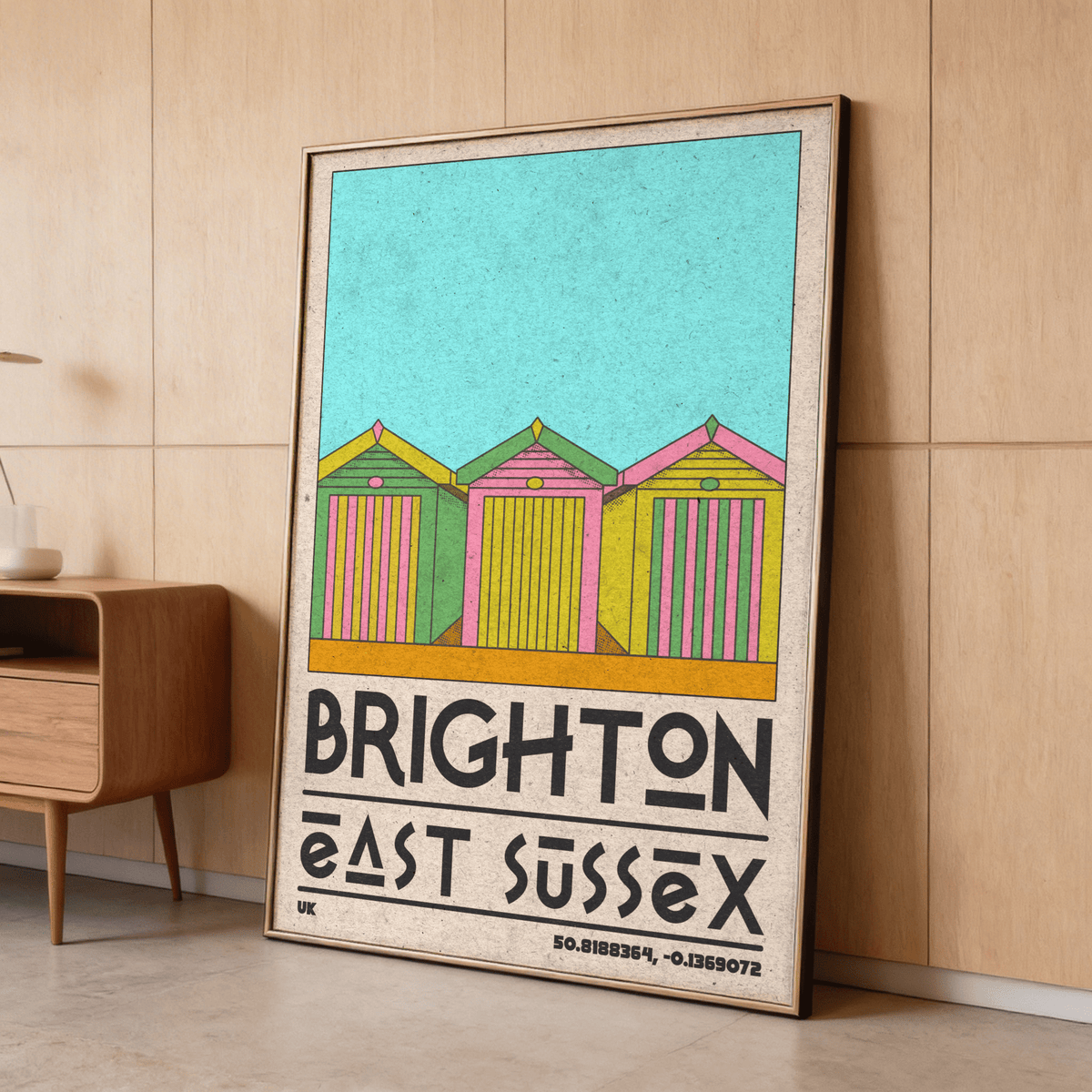 Framed Brighton Travel Print with colourful retro beach huts leaning against wooden wall near cabinet