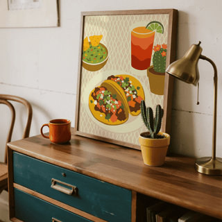 Print leaning on a wooden sideboard showing tacos art print with green cactus and orange mug nearby