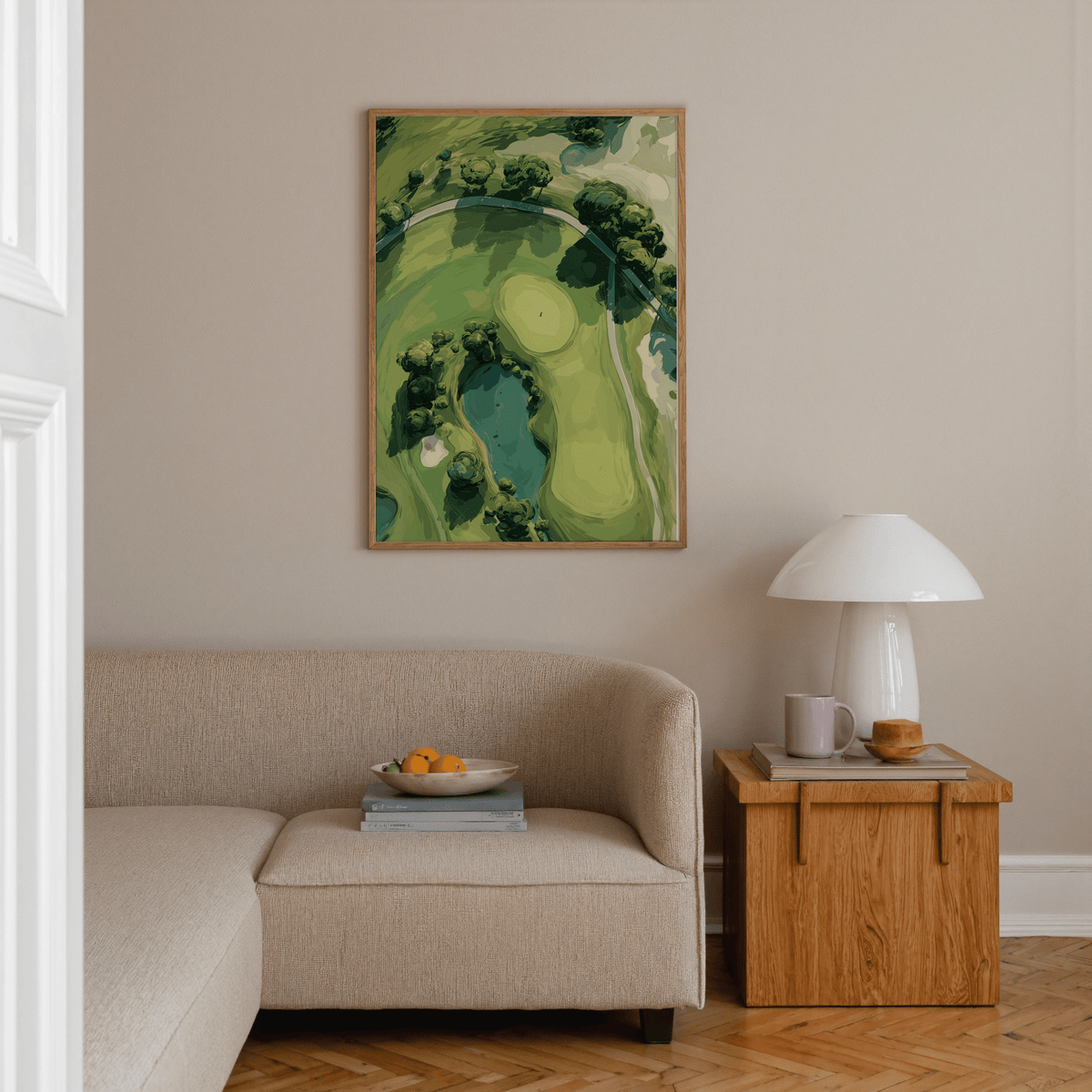 Aerial Golf Landscape Poster on a beige wall above a beige sofa with a wooden side table and lamp