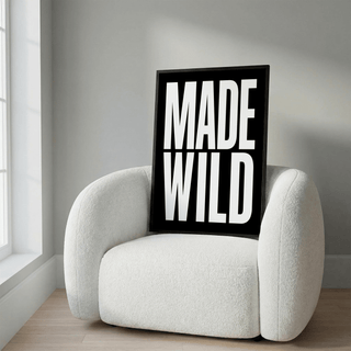 Framed Made Wild art print with bold white text on black leaning on a cream armchair