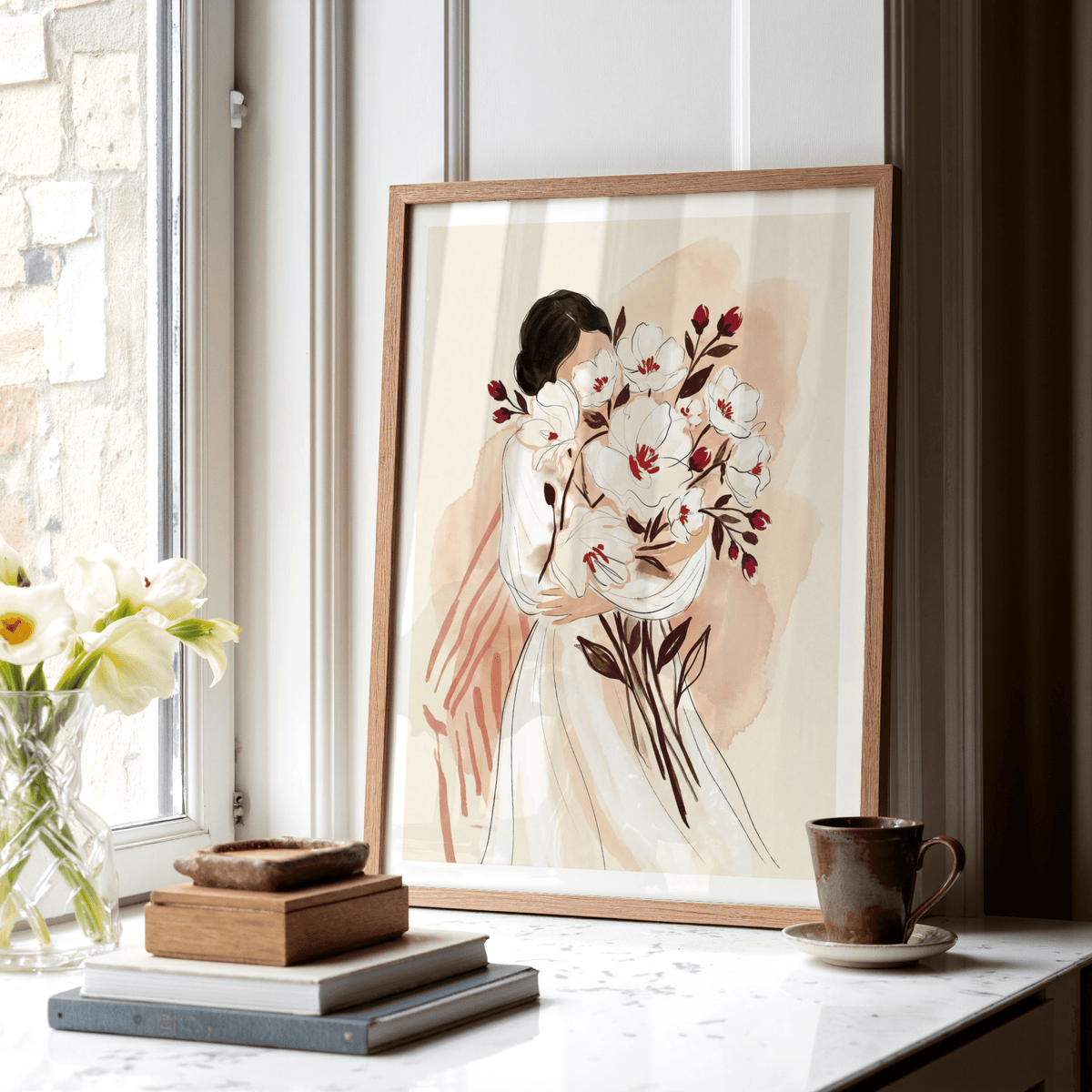 Woman Holding Flowers print leaning on a window sill with a brown cup and books nearby