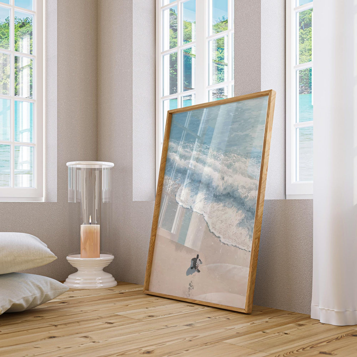 Print leaning on a wooden floor showing a minimalist baby sea turtle on a sandy beach next to blue waves with a candle nearby