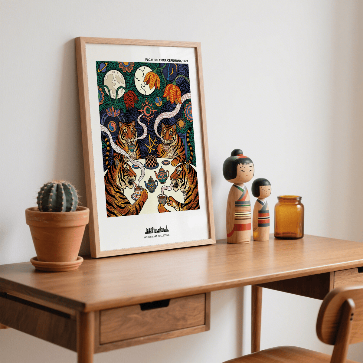 Framed Tiger Tea Ceremony print leaning on a wooden desk with a small cactus and dolls nearby