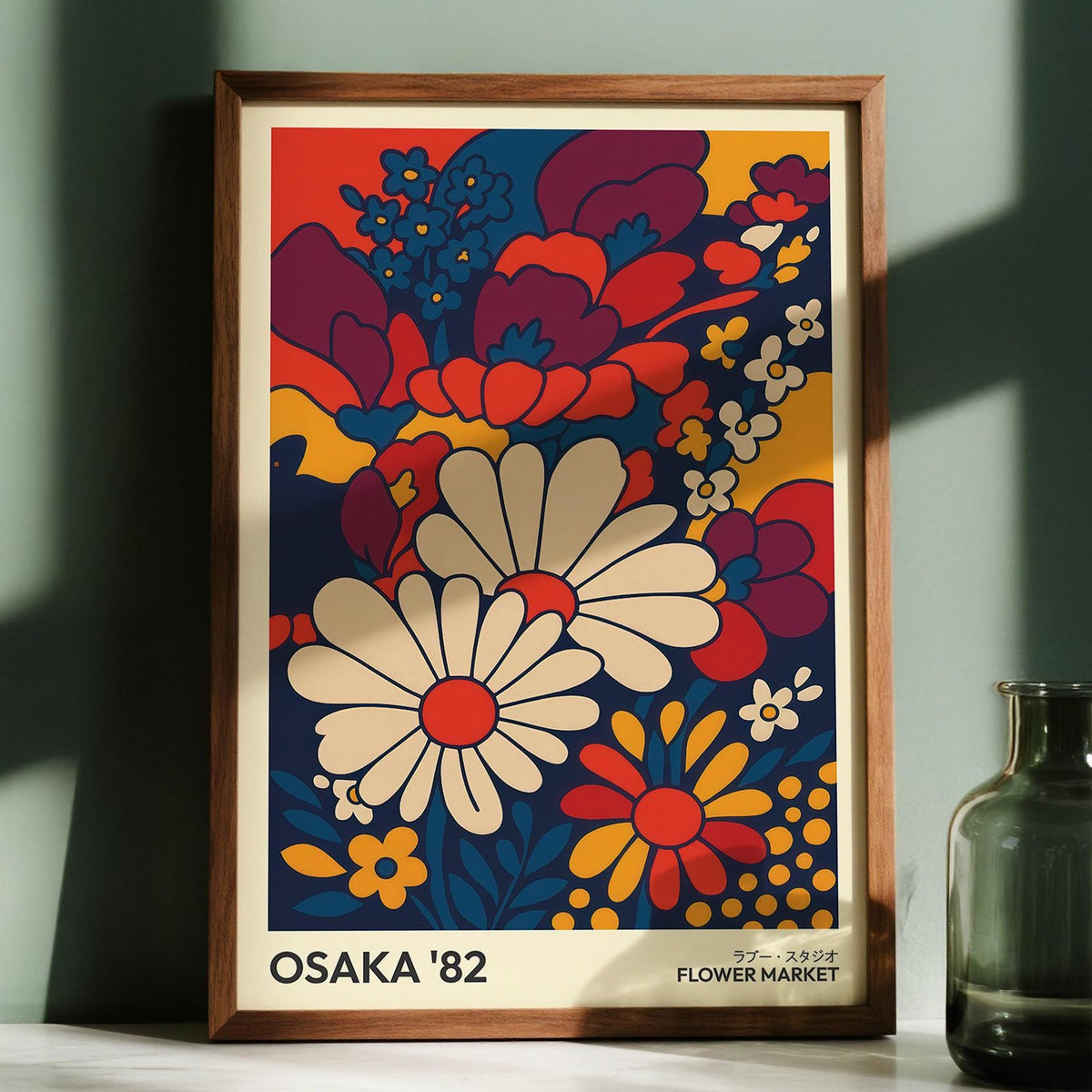 Retro wall art prints of daisy flowers in cream red and blue framed and leaning against a green wall with a green glass vase nearby
