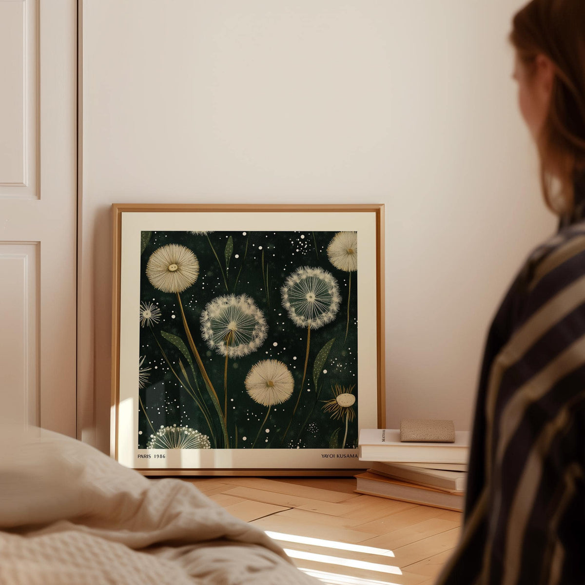 Square wall art featuring white dandelion seed heads in botanical illustration style leaning on wooden floor near books