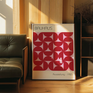 Print leaning on a wooden floor with Bauhaus artworks featuring a red geometric pattern near a green leather sofa