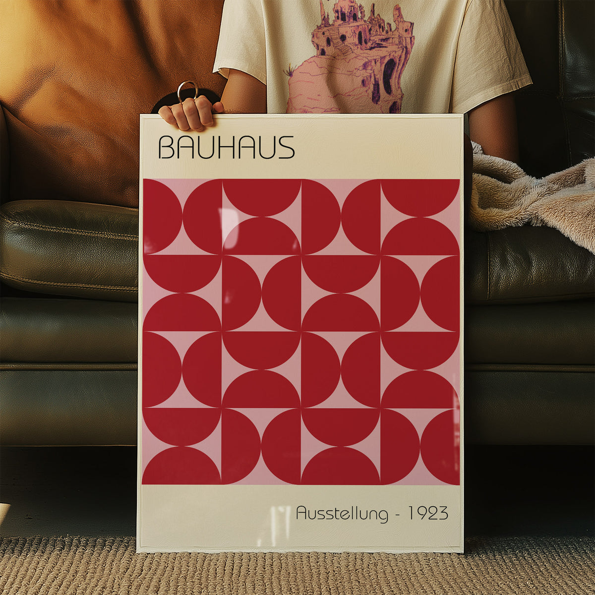 Framed Bauhaus artworks with red geometric pattern held in front of a dark green leather sofa