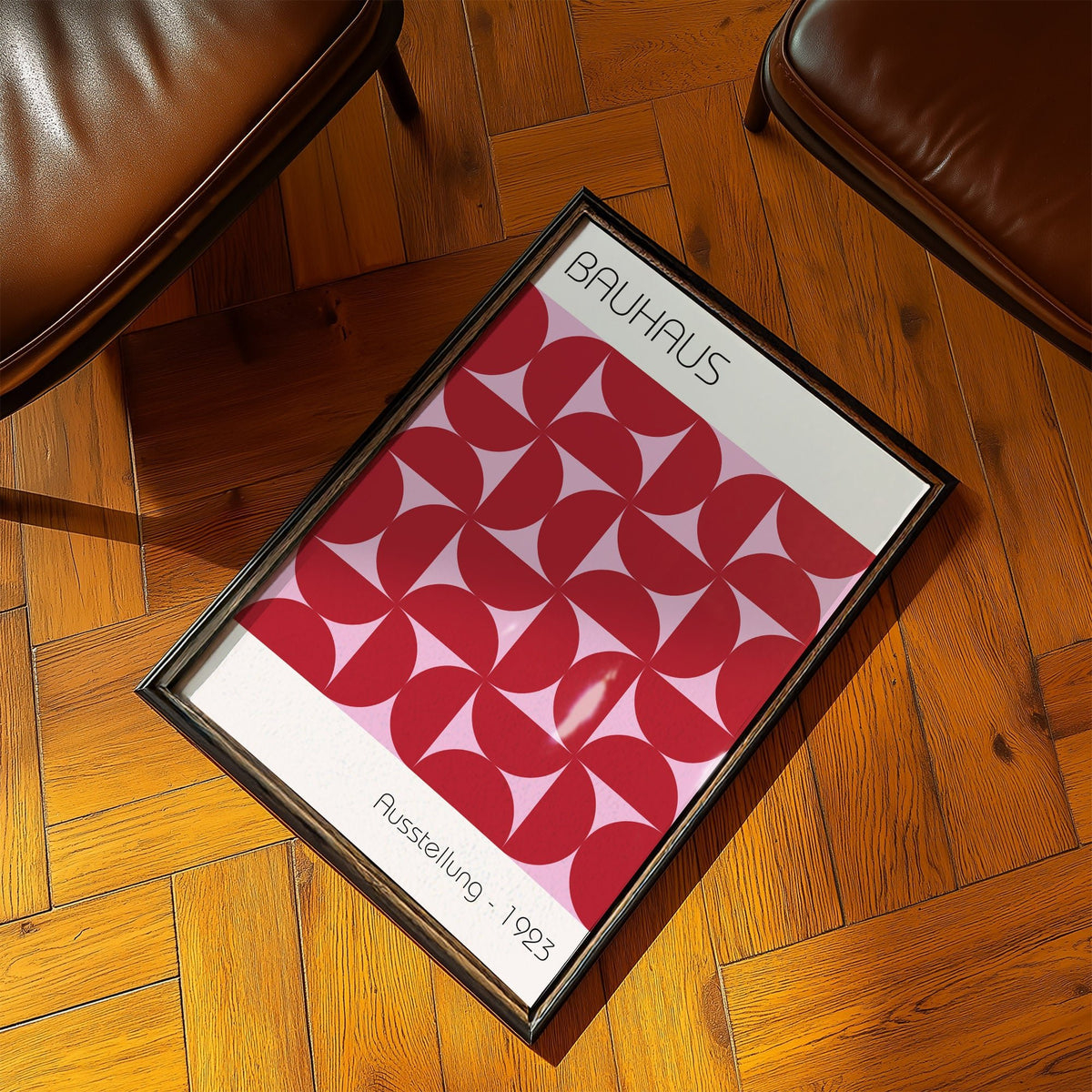 Framed Bauhaus artworks print with a red geometric pattern on a parquet floor between two brown chairs