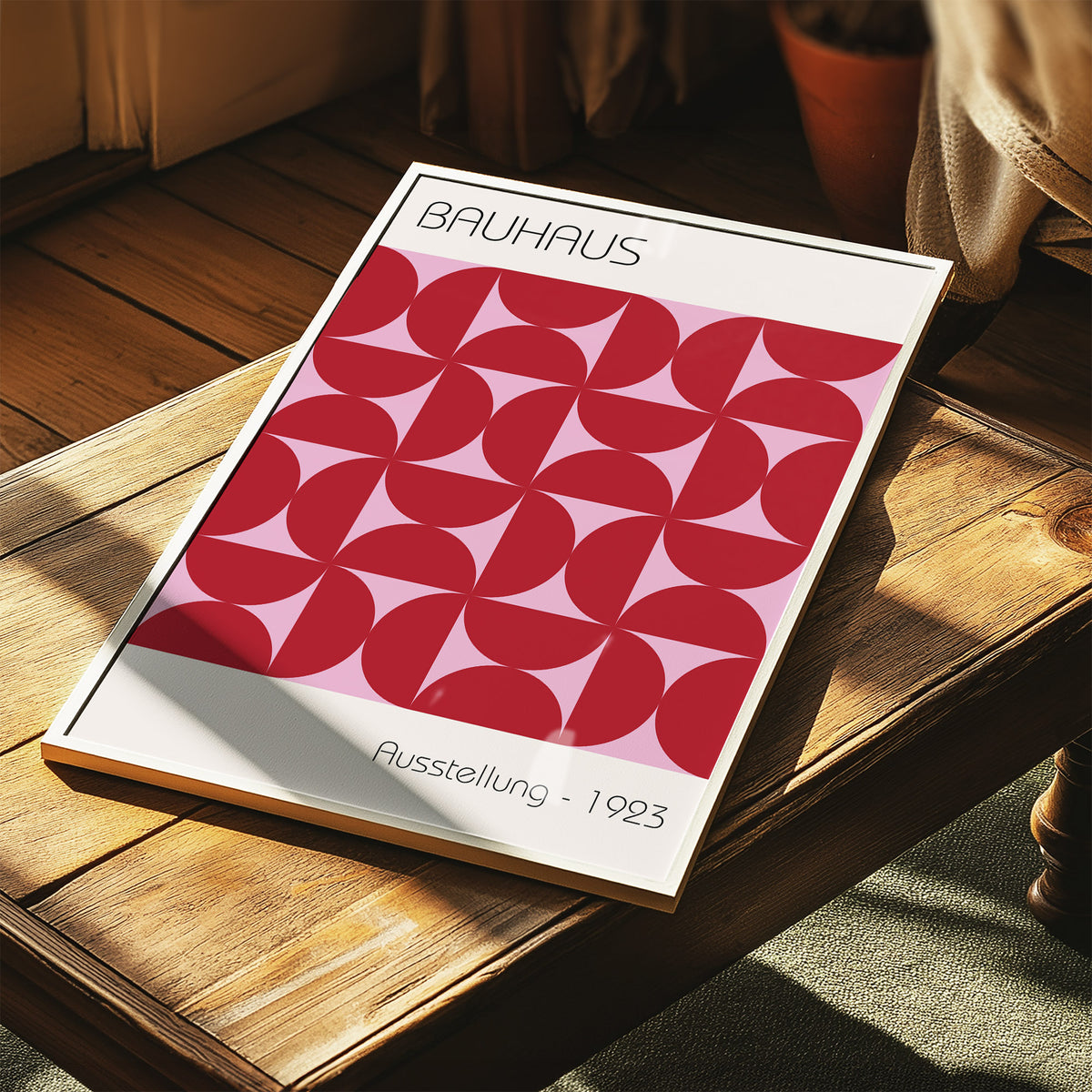 Framed Bauhaus artworks with red geometric pattern and pale pink background leaning on wooden table