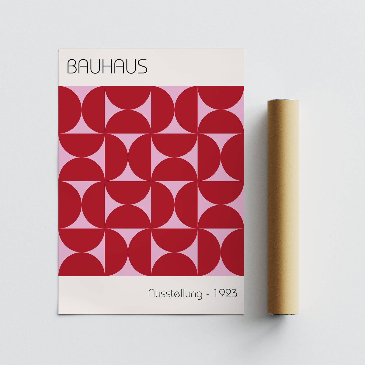 Bauhaus artworks print with a red geometric pattern and pink background lying flat beside a packaging tube