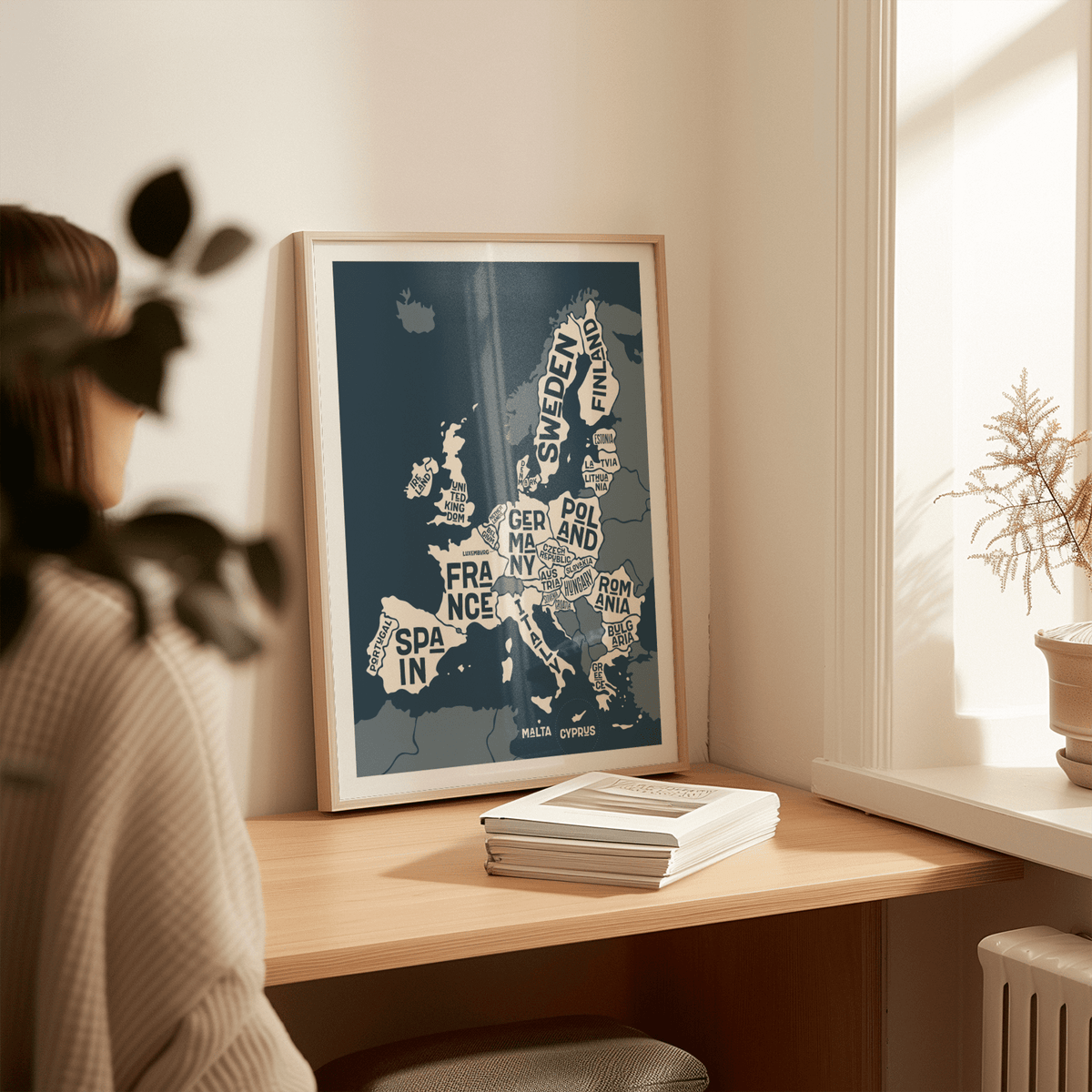 Europe Map Print leaning on a desk with white and dark blue minimalist typography next to a potted plant