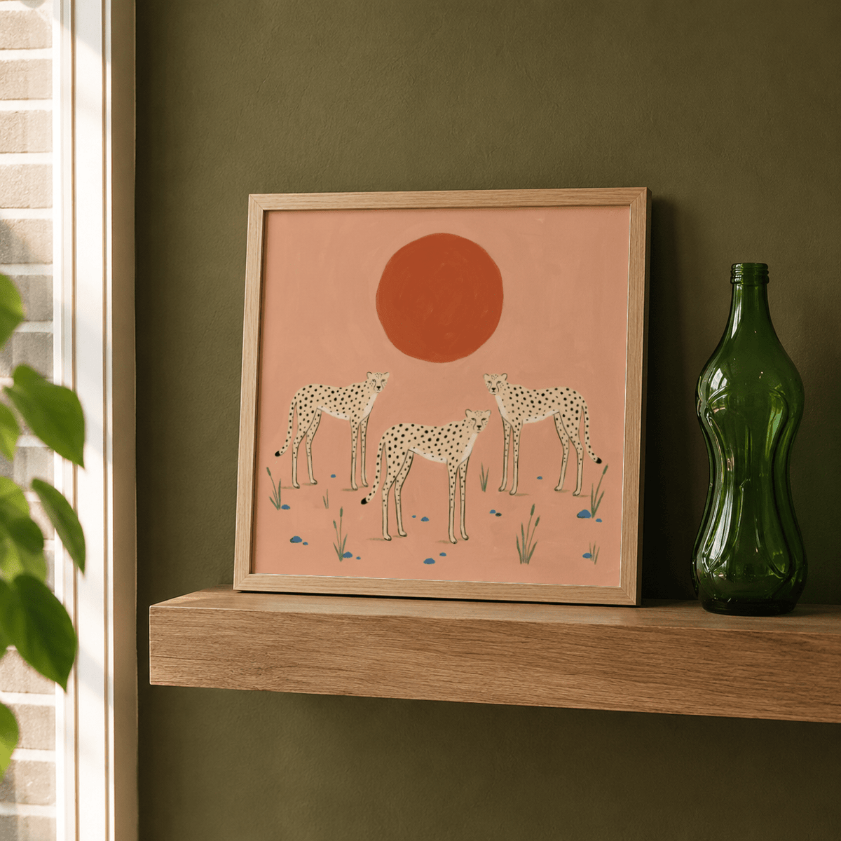 Print leaning on a shelf with three cheetahs and a large red sun with muted pink background next to a green glass bottle