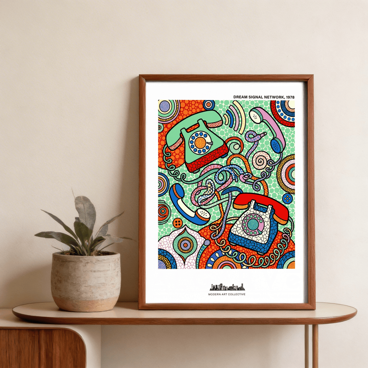 Framed vintage telephone art print with colourful rotary phones leaning against a beige wall beside a potted plant