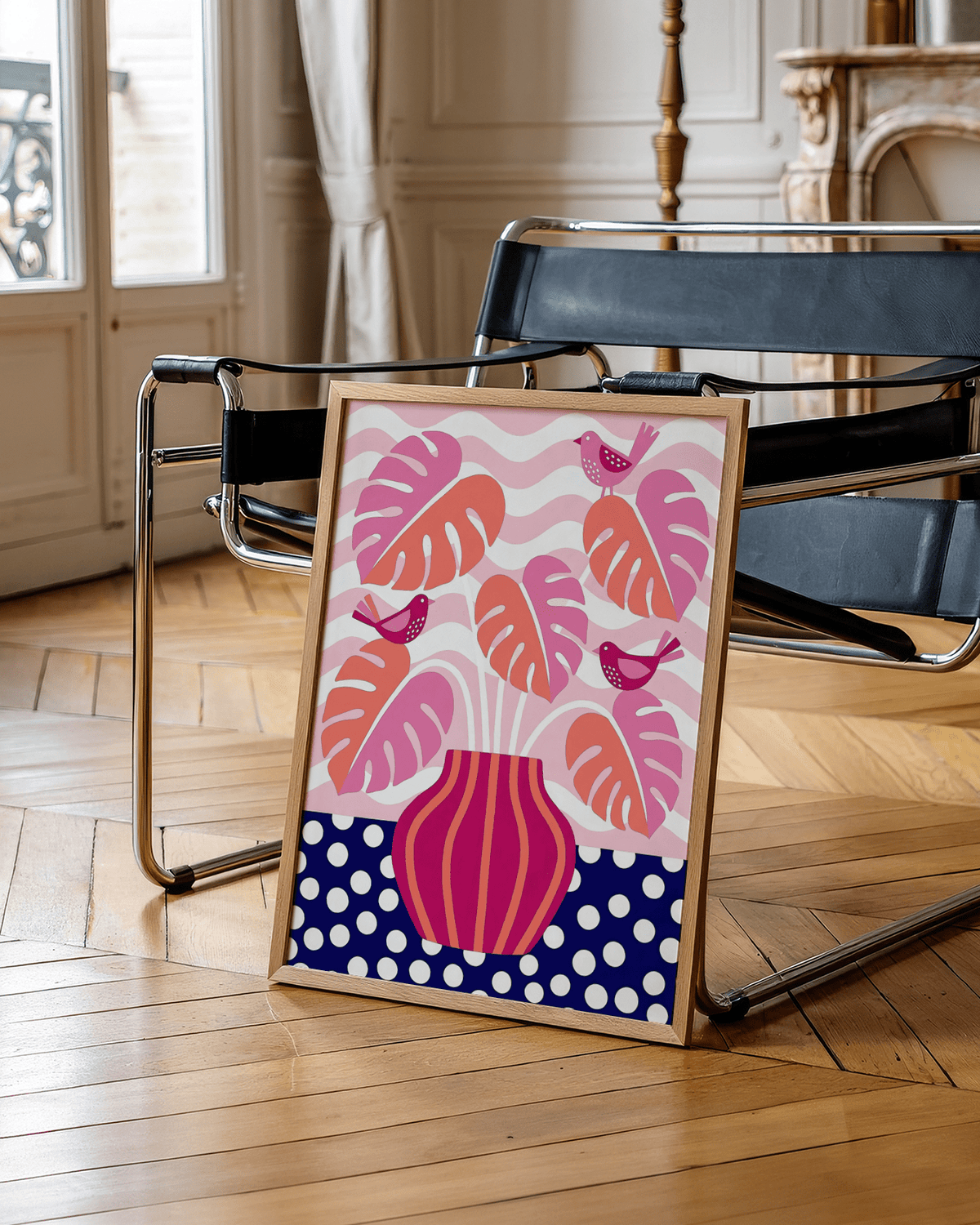Tropical Plant wall art with pink and orange monstera leaves and birds leaning on a black chair in a room