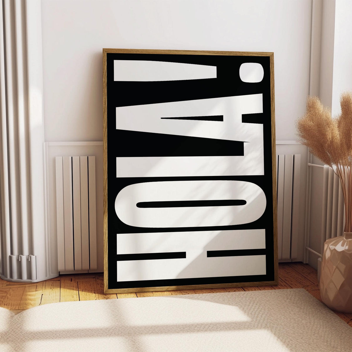 Poster with bold HOLA text in white on black leaning on a wooden floor near dried plants