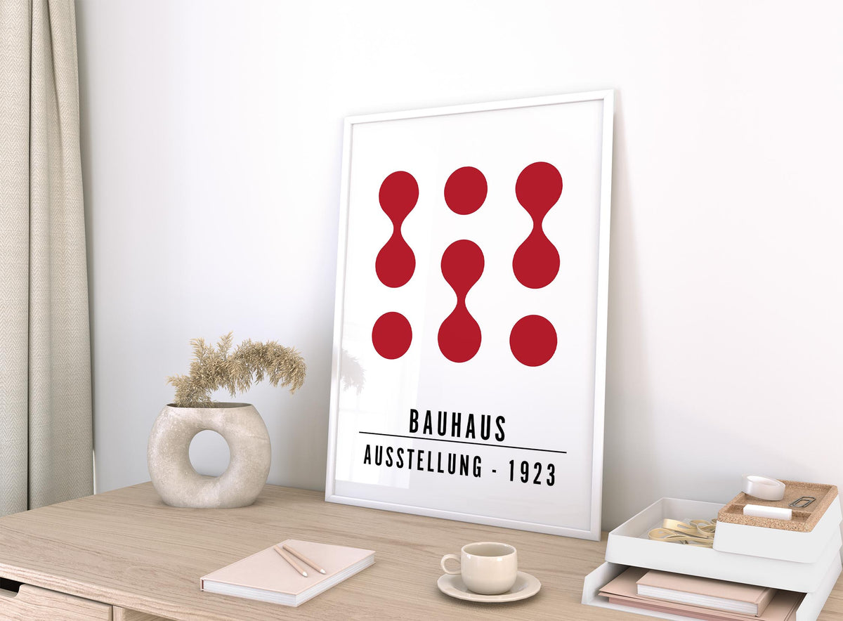 Artwork for Office Walls leaning on a desk with abstract red shapes and a beige vase with dried flowers