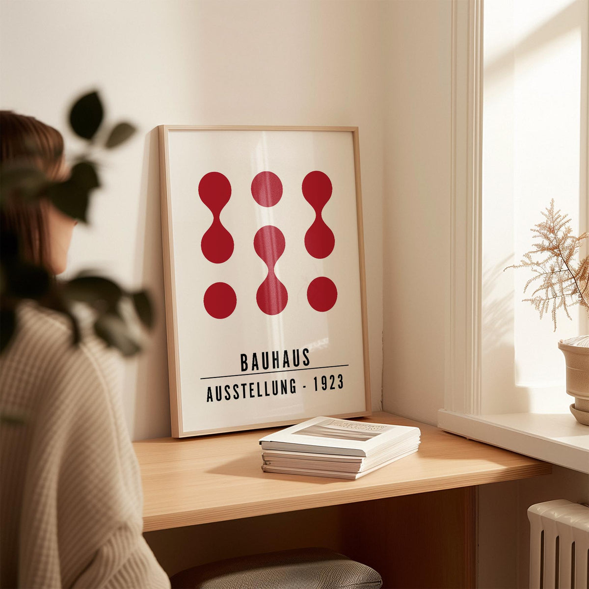 Artwork for Office Walls leaning print with red abstract shapes on a desk with books and a plant