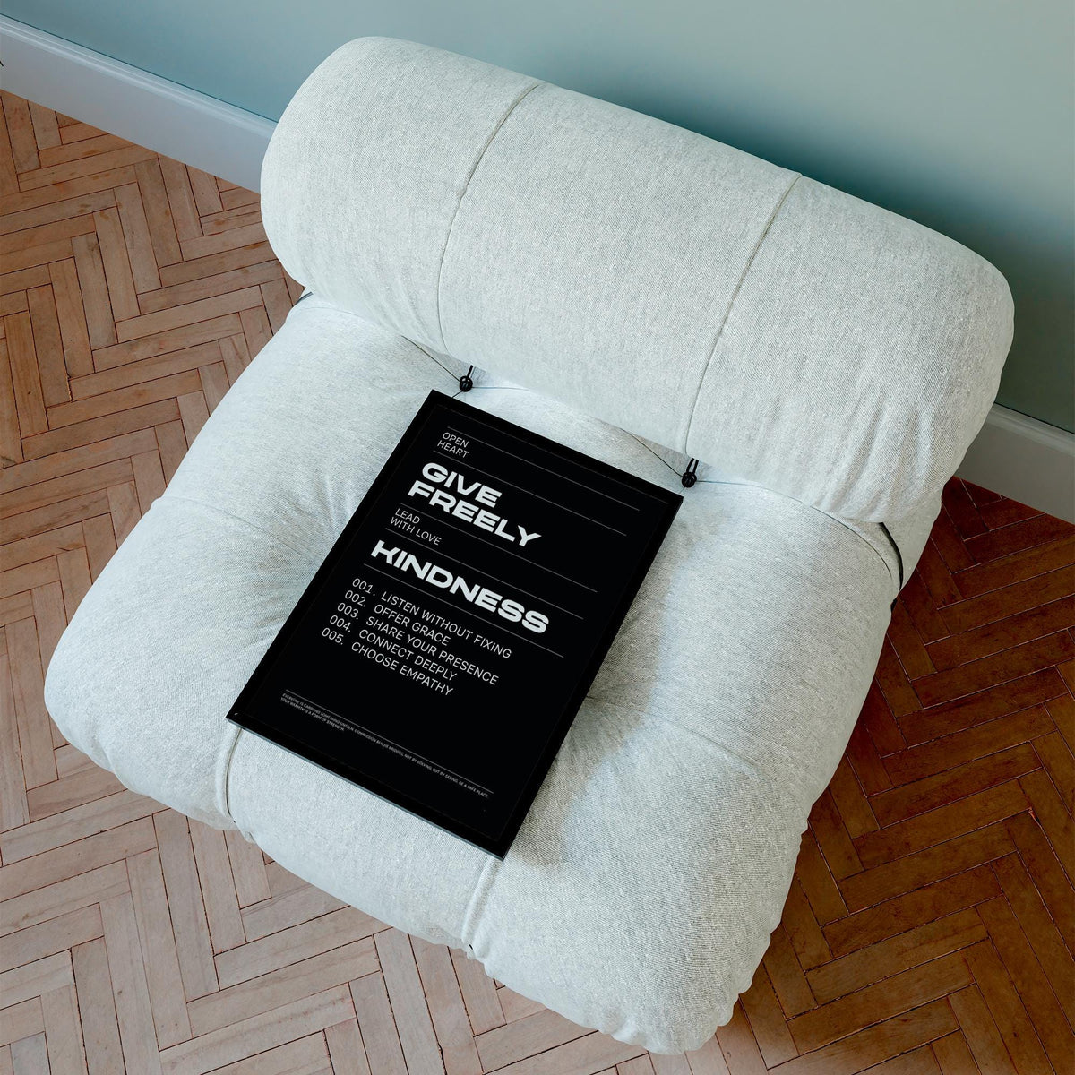 Art with Quote print with white text on black lying on a light grey cushioned chair