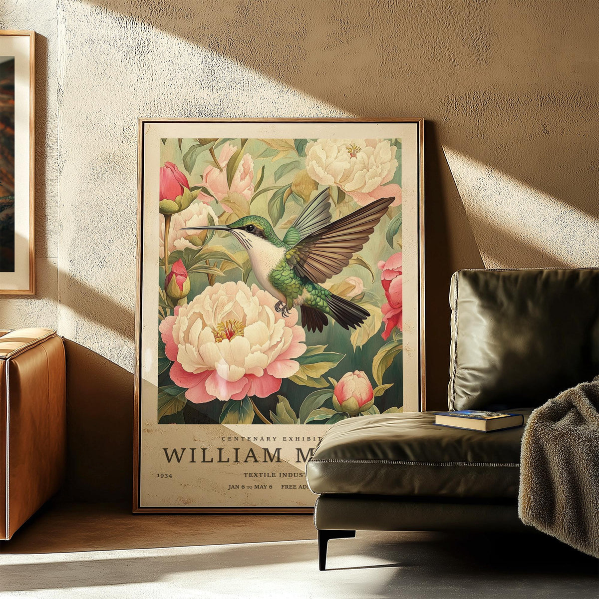 Print leaning on floor of hummingbird prints featuring a bird with green wings and pink peonies beside a leather sofa