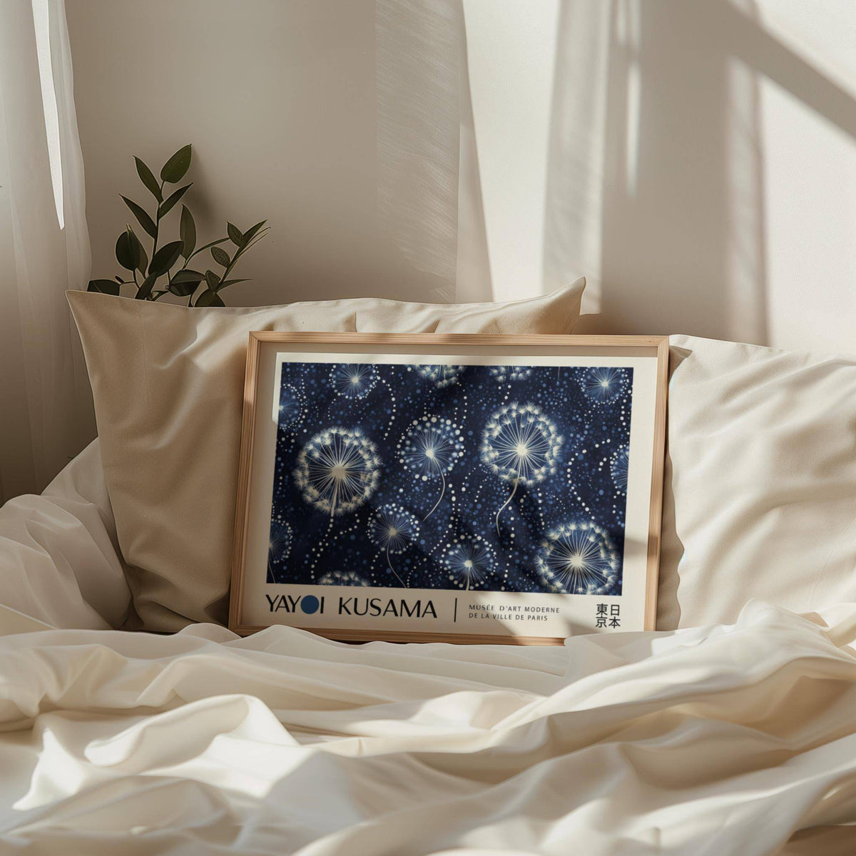 Print of dandelion seed heads in blues and whites leaning on a bed with cream bedding and cushions and a plant nearby