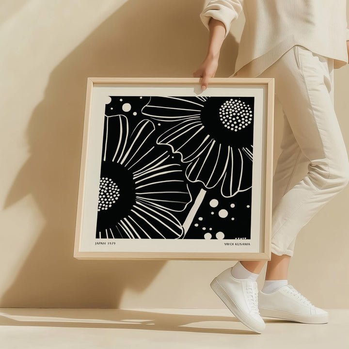 Framed close-up of black white floral art featuring minimalist daisy flowers with dots held by a person in white clothes