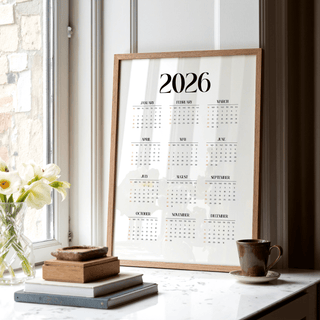 Minimalist wall calendar framed leaning on a window ledge with books and a cup nearby