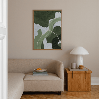 Abstract Green Art Print with layered green and pale blue shapes above a beige sofa with a wooden side table and lamp