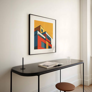 Framed print of modernist building illustration in bright colours above a black desk with a candle and book