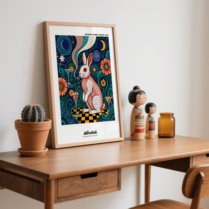 Framed Colorful Rabbit Art Print leaning on a wooden desk with two wooden dolls and a cactus plant
