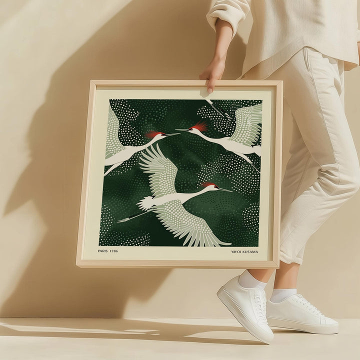 White Crane Birds Art showing a minimalist illustration of white cranes with red heads and green background held by a person