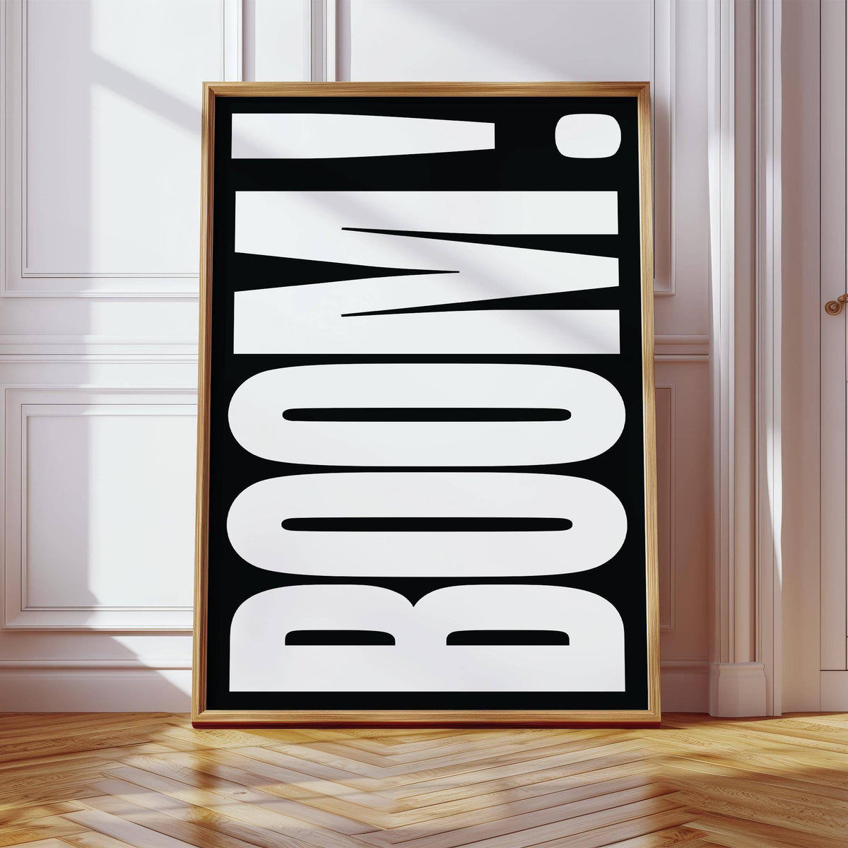 Framed BOOM typography wall art in white on black leaning on wooden parquet floor