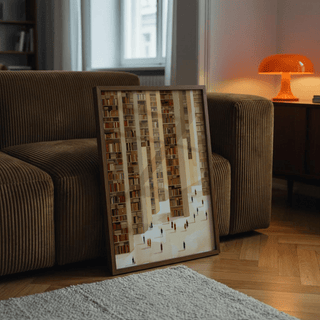Framed Library Art Print leaning on a brown sofa with orange lamp in the background