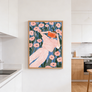 Woman Reading Art Print in a wooden frame showing a person in a striped outfit reading among pink flowers in a kitchen