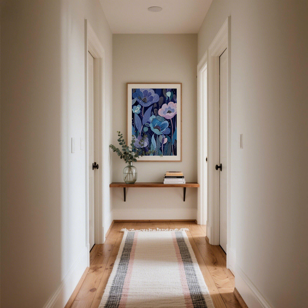 Print on a wall in a hallway with wooden floor and a shelf holding a vase and books
