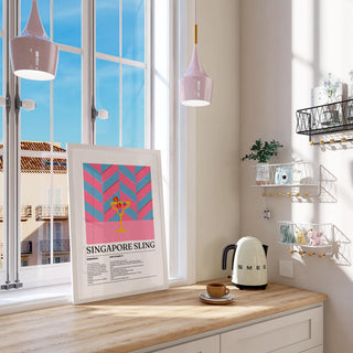 Print leaning on a shelf of singapore sling drinks art with pink blue chevron design beside a cream kettle