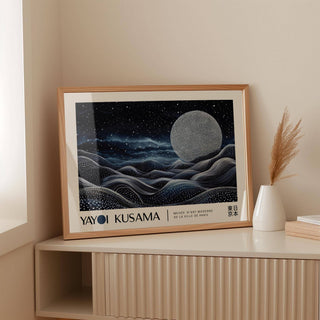 Framed Space Art Wall print of moon over abstract waves in dark blues leaning on a shelf with a white vase