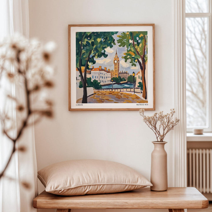 Print on a wall in a neutral room of a big Ben clock tower illustration with green trees and blue sky above a beige cushion on a wooden