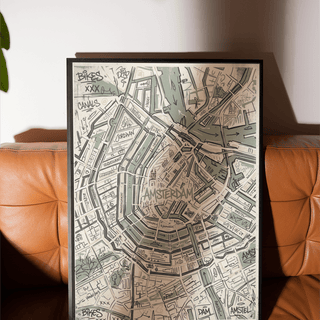 Framed Amsterdam map art print with a minimalist line-art style resting on a brown leather sofa