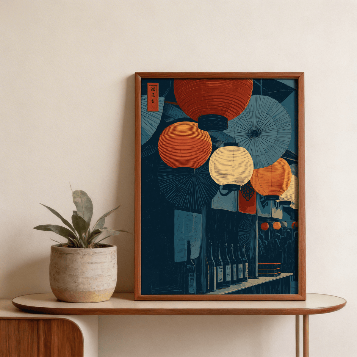 Framed Japanese Lantern Wall Art with red and cream lanterns on a wooden shelf next to a small plant