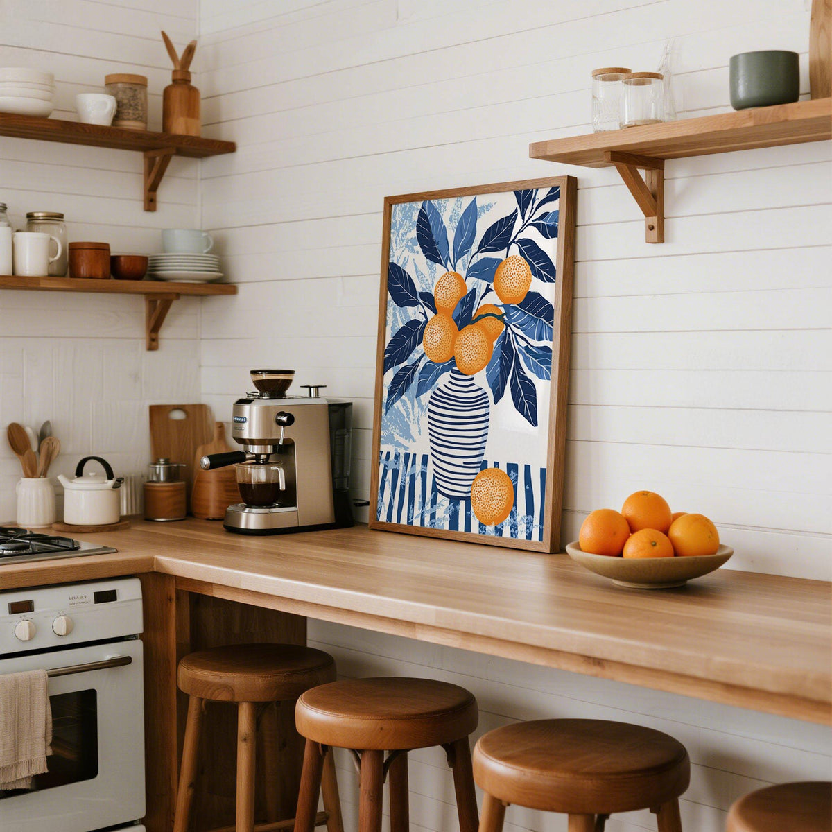 Print leaning on kitchen counter of a vase with blue leaves and oranges with bowl of oranges nearby