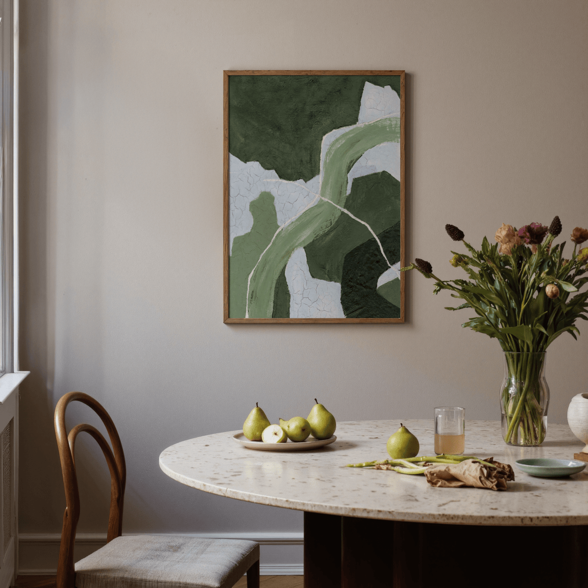 Abstract green art print with flowing shapes framed above a dining table with fruit and flowers